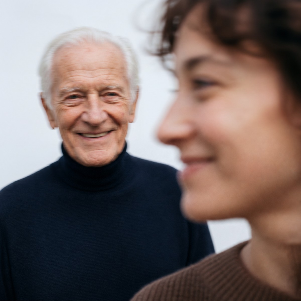 An older man smiling warmly while a caregiver sits beside him